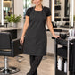 SalonCapes black waterproof chemical apron worn by a professional stylist in a modern salon