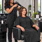 Black crepe zipper-front salon robe worn during professional blow-dry service