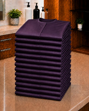 Stack of 13 folded eggplant iridescent snap-front salon robes for Baker’s Dozen bulk ordering