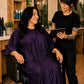 Client seated in an eggplant iridescent snap-front salon robe while consulting with a stylist holding a tablet