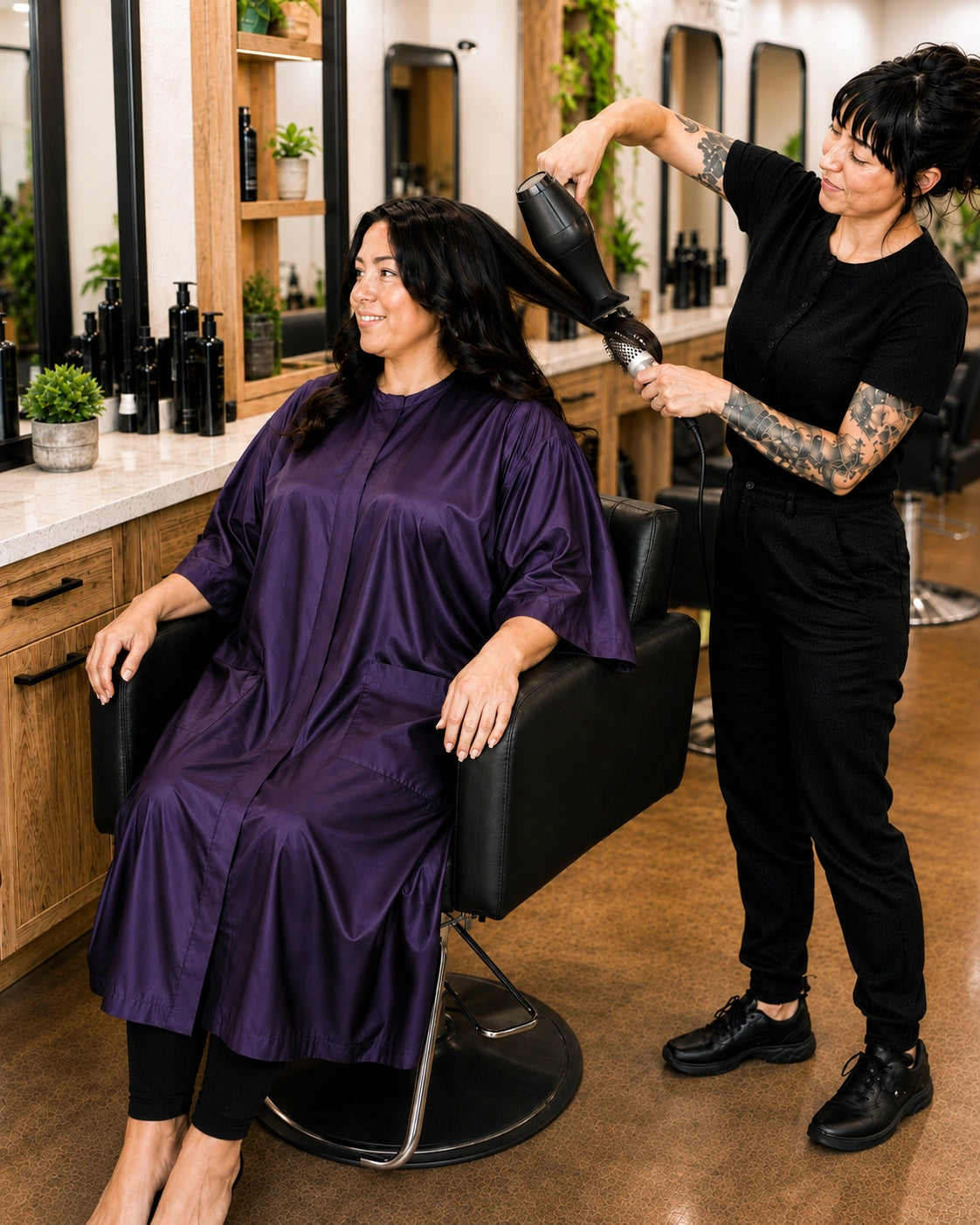 Client wearing an eggplant iridescent snap-front salon robe during a professional blow-dry service