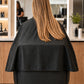 Black SalonCapes chemical cape wrapping around salon chair for extended client and chair coverage