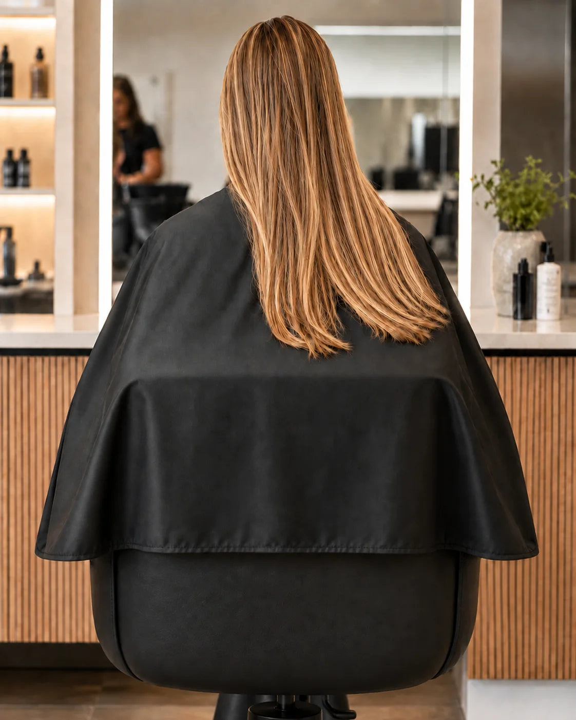 Black SalonCapes chemical cape wrapping around salon chair for extended client and chair coverage
