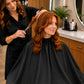 Stylist cutting hair with client protected by a black SalonCapes crepe cutting cape