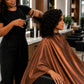 Side view of stylist cutting hair with client protected by a copper iridescent SalonCapes cutting cape