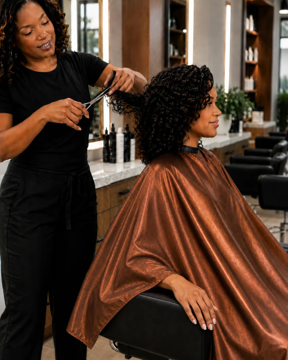 Side view of stylist cutting hair with client protected by a copper iridescent SalonCapes cutting cape
