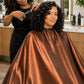 Stylist cutting hair with client wearing a copper iridescent SalonCapes cutting cape with full coverage