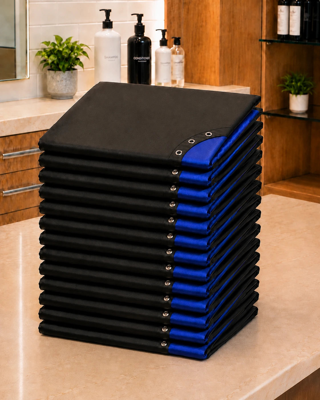 Stack of 13 royal blue and black SalonCapes reversible chemical capes representing the Baker’s Dozen bulk purchase option