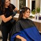Stylist performing a color service with client protected by a royal blue and black SalonCapes reversible chemical cape