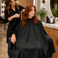 Client wearing a black SalonCapes crepe cutting cape with full salon-chair coverage