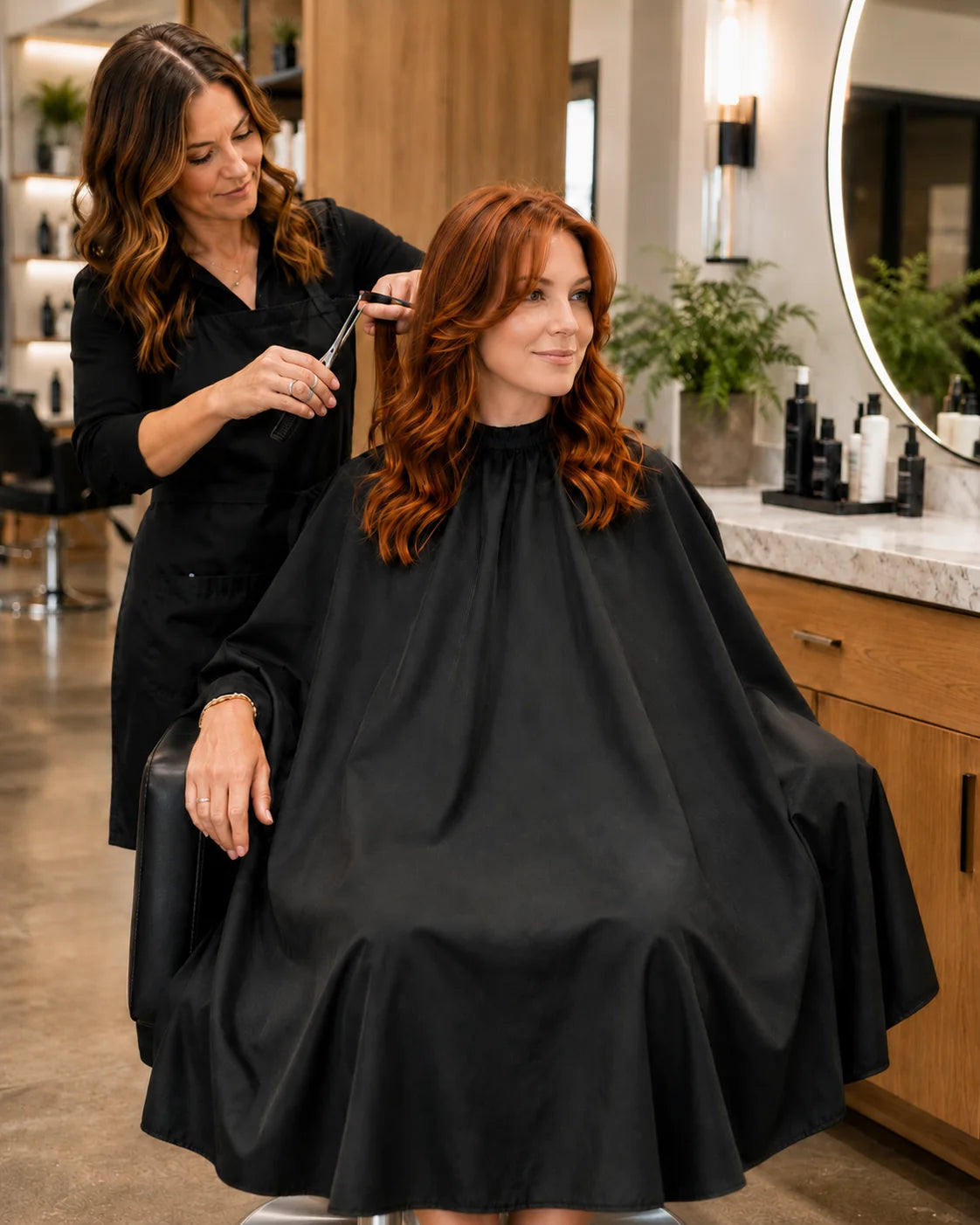 Client wearing a black SalonCapes crepe cutting cape with full salon-chair coverage